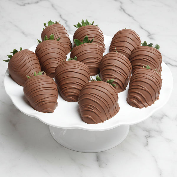 Chocolate-covered strawberries on a white cake stand with a light wooden background